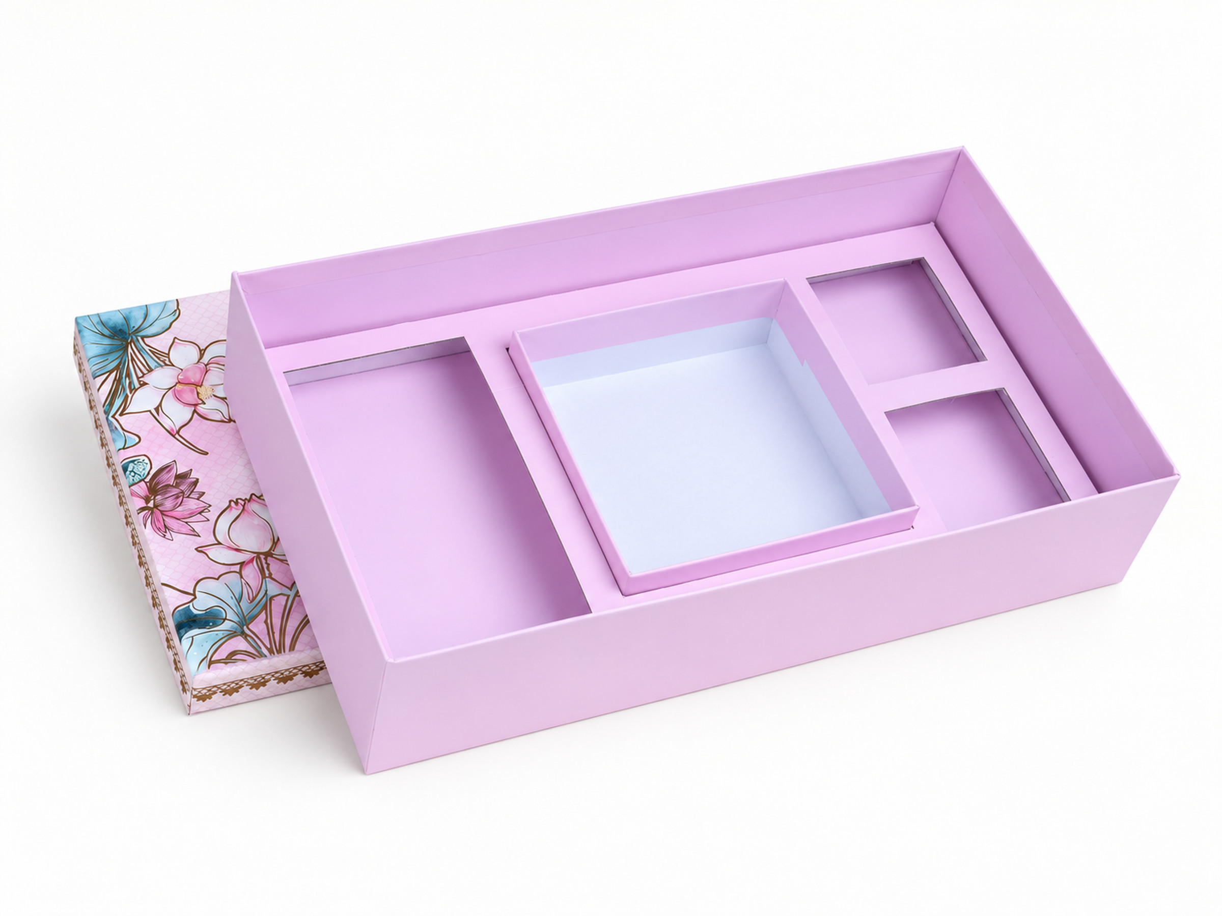 Open pink gift box showing a long left compartment, a central tray and two right-hand compartments, with the floral lid behind.
