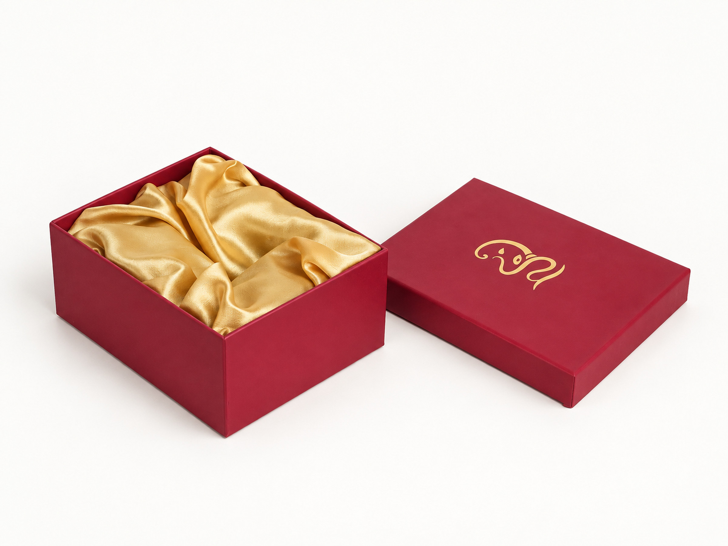 Open burgundy square gift box with gold satin lining and a matching lid bearing a gold Ganesha motif.