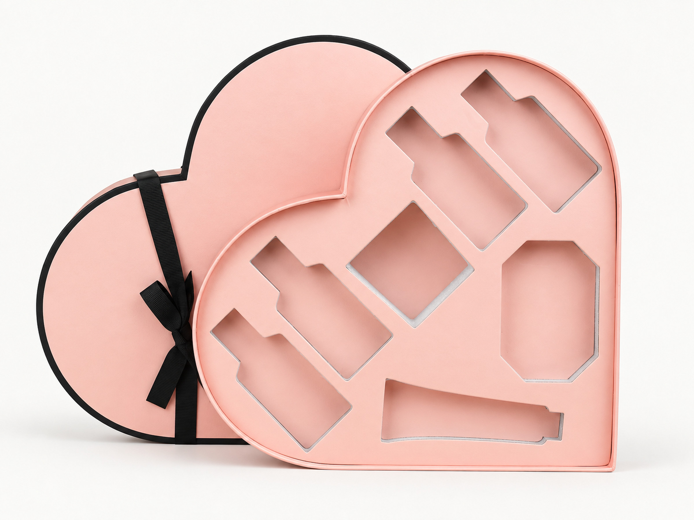 Open blush pink heart-shaped gift box with fitted bottle and accessory cutouts, shown with its matching lid and black ribbon.