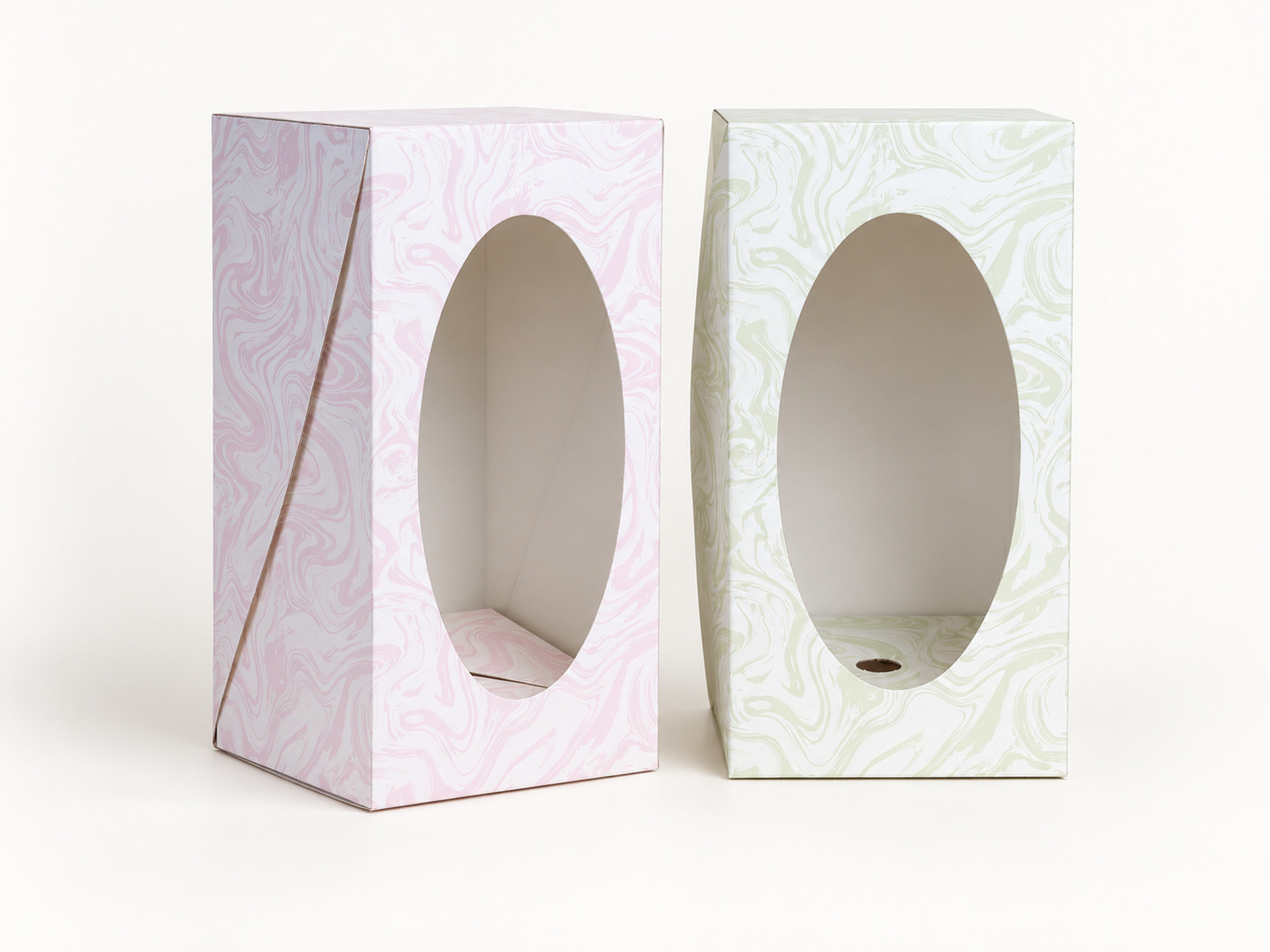 Blush pink and sage green swirl-pattern upright gift boxes with large oval windows, shown side by side.