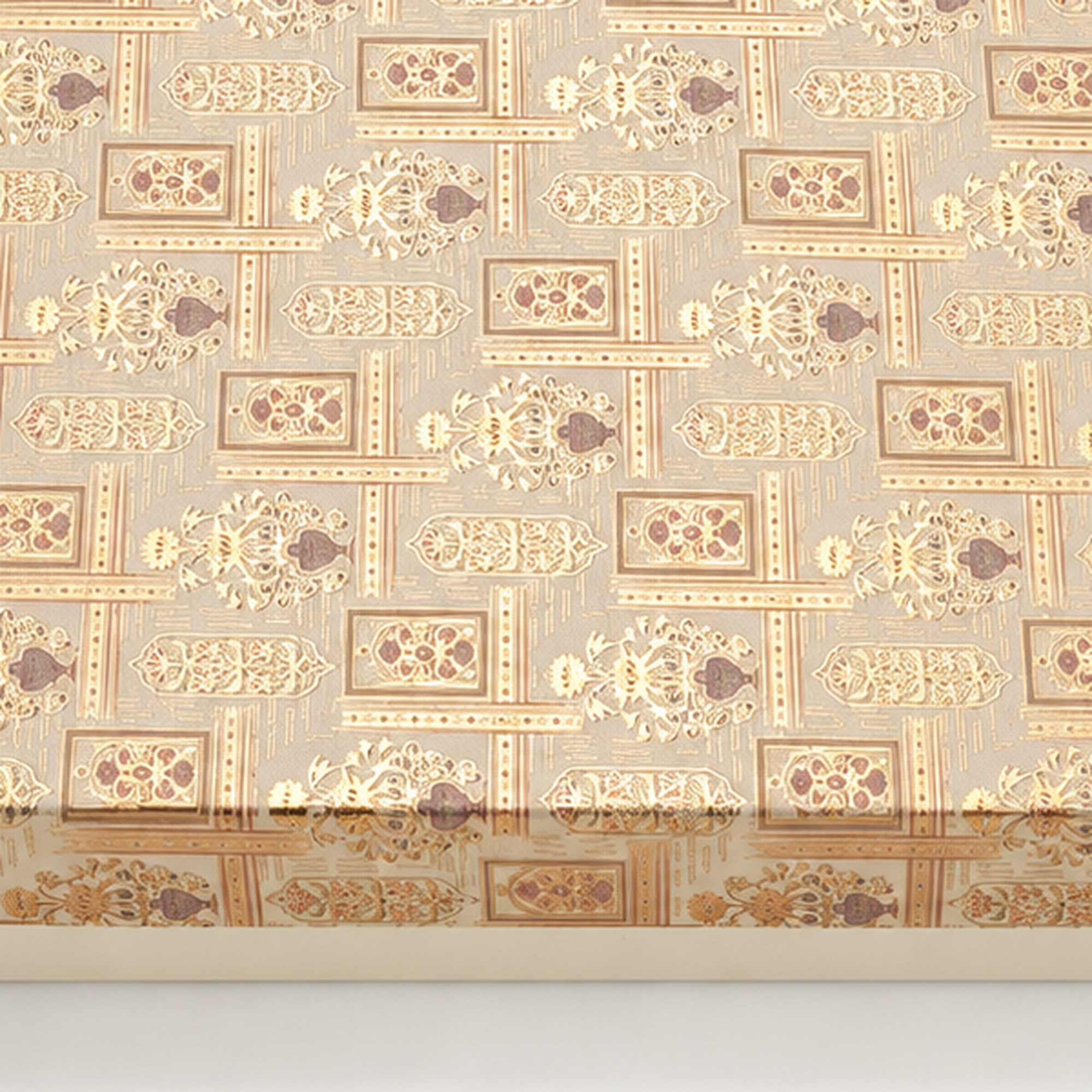 Close-up of the repeating gold and muted mauve artwork on the ivory gift-box lid.