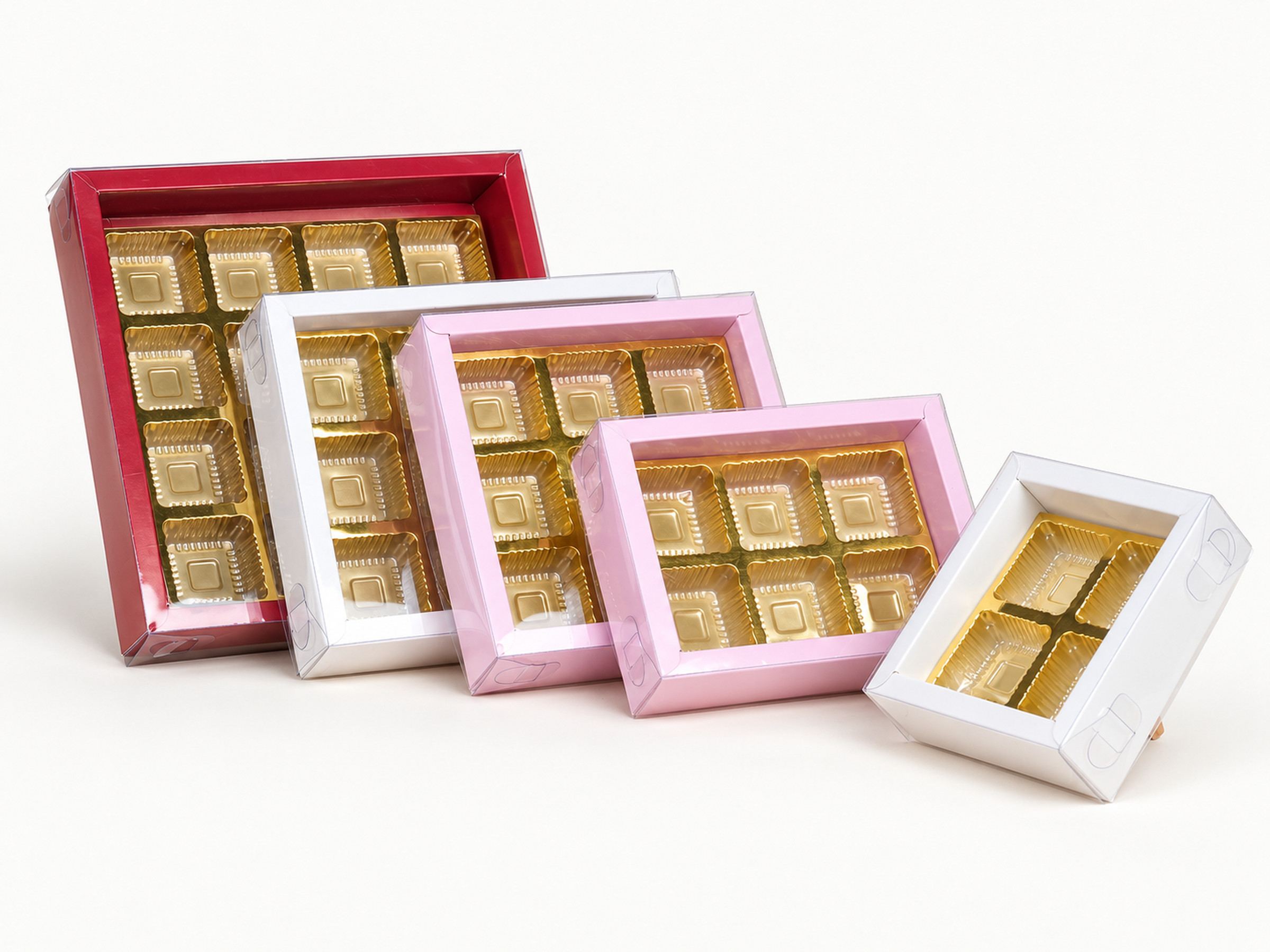 Five clear-lid chocolate boxes in burgundy, white and pastel pink with gold-coloured inserts, shown in assorted sizes. Supplementary reference only; product identity, sizes and availability require confirmation.