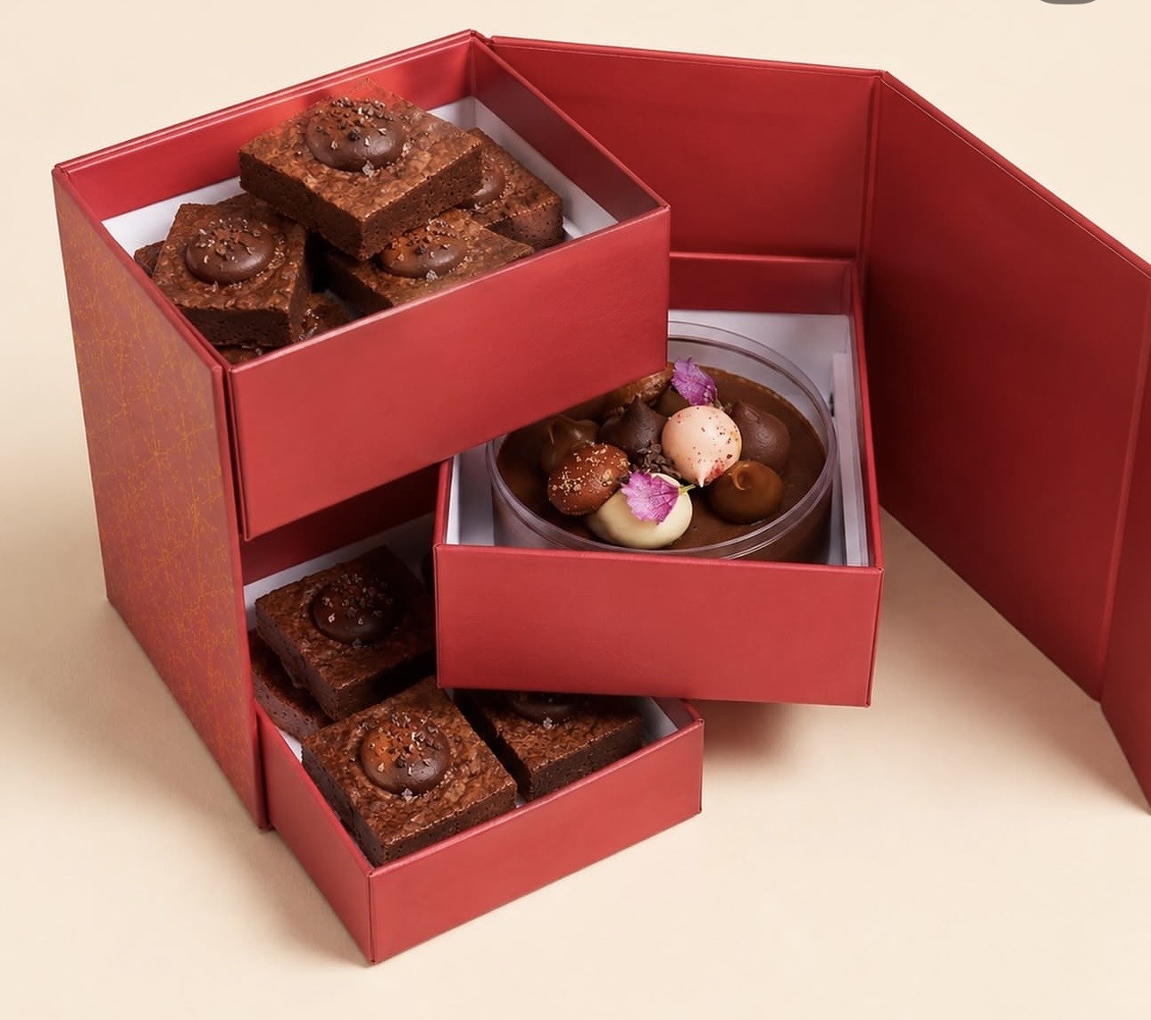 Open three-tier drawer gift box with red trays and a fold-out door, shown with brownies and chocolates as display props.